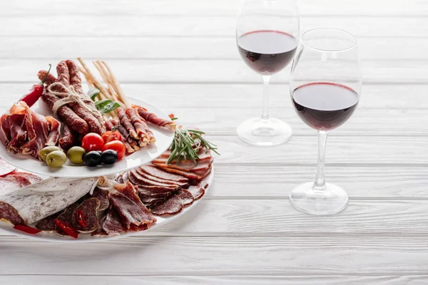 Close up view of glasses of red wine and delicious meat snacks on white wooden tabletop — Stock Photo