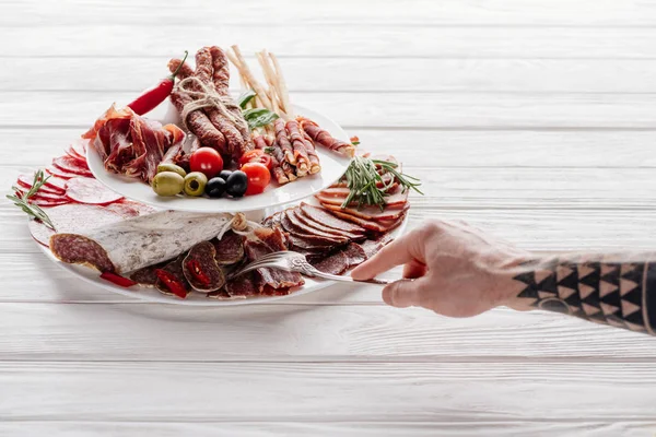 Vista parcial del hombre probando bocadillos de carne en la mesa de madera blanca - foto de stock