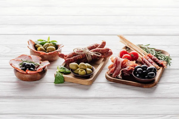 Composición de alimentos con varios aperitivos de carne, aceitunas y hojas de albahaca en la superficie de madera blanca - foto de stock