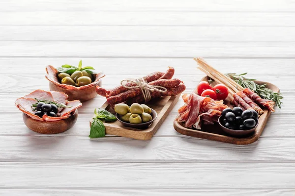 Composition alimentaire avec divers apéritifs à base de viande, olives et feuilles de basilic sur une surface en bois blanc — Photo de stock