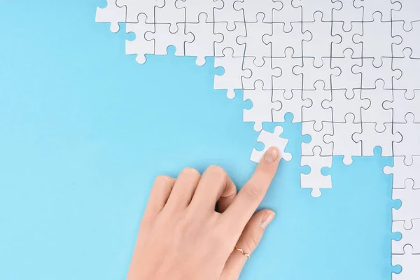 Vista parcial de la mujer con piezas de rompecabezas blancos sobre fondo azul - foto de stock