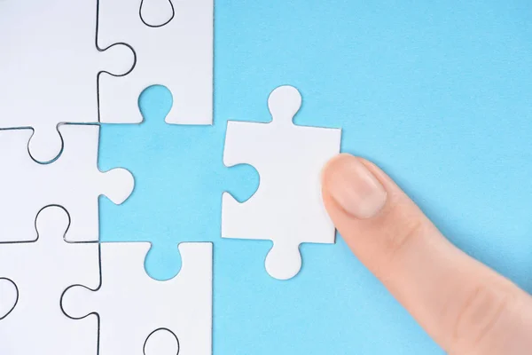 Plan recadré de femme pointant vers des pièces de puzzles blancs sur fond bleu — Photo de stock