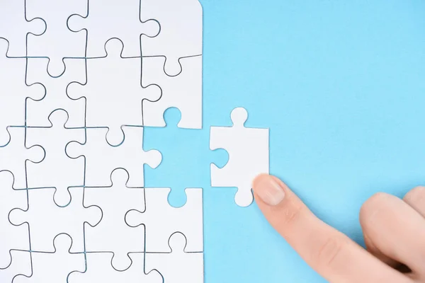 Teilansicht einer Frau, die auf weiße Puzzleteile auf blauem Hintergrund zeigt — Stockfoto