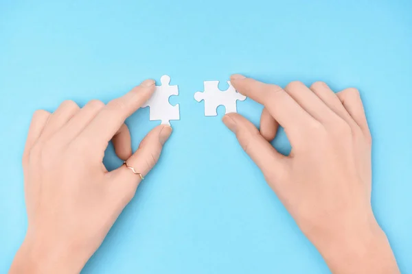 Partial view of woman holding white puzzles pieces on blue background — Stock Photo