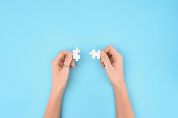 Cropped shot of woman holding white puzzles pieces on blue background — Stock Photo