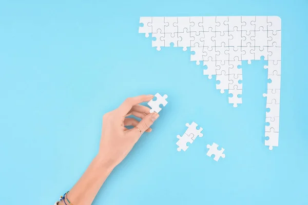 Cropped shot of woman holding white puzzles piece on blue background — Stock Photo