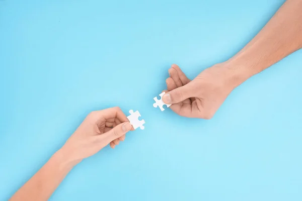 Cropped shot of man and woman with white puzzle pieces on blue backdrop, cooperation concept — Stock Photo