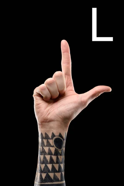 Vista recortada de la mano tatuada que muestra la letra latina - L, lenguaje de signos, aislado en negro - foto de stock