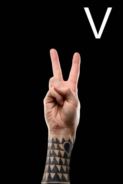 Vista parcial de la mano masculina tatuada que muestra la letra latina - V, lenguaje sordo y mudo, aislado en negro - foto de stock