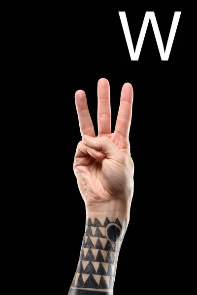 Partial view of tattooed male hand showing latin letter - W, deaf and dumb language, isolated on black — Stock Photo