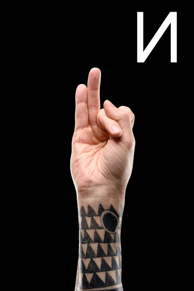 Vista recortada de mano masculina tatuada mostrando letra cirílica, lenguaje sordo y mudo, aislado en negro - foto de stock