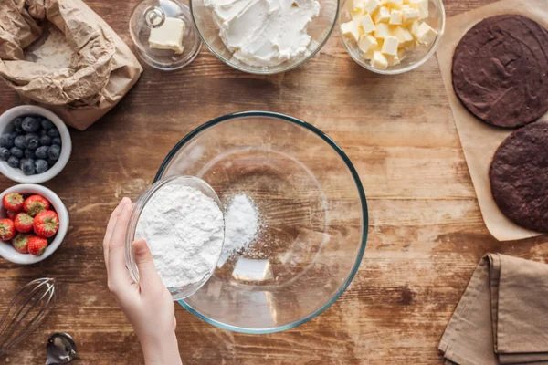 Vue partielle du dessus de la femme tenant la farine et préparant la pâte pour un délicieux gâteau fait maison — Photo de stock