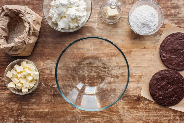 Vista superior da tigela de vidro vazia e ingredientes para delicioso bolo caseiro na mesa de madeira — Fotografia de Stock