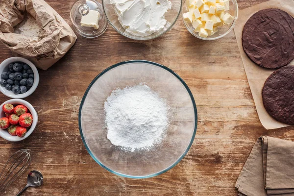 Vue du dessus du bol avec de la farine et des ingrédients pour gâteau maison sucré sur la table — Photo de stock