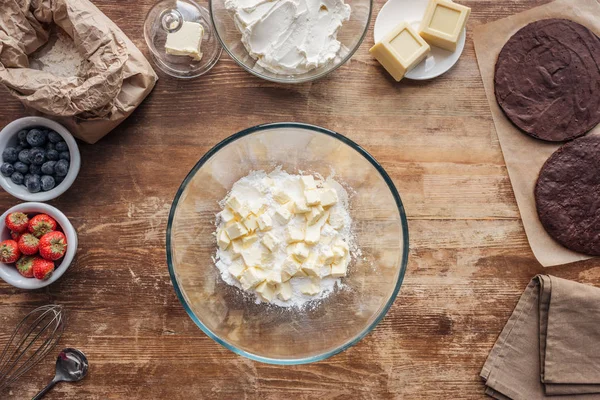 Vista superior del tazón con harina y mantequilla e ingredientes para pastel casero en la mesa - foto de stock