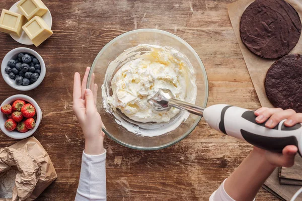 Vista superior parcial de la mujer mezclando crema para deliciosa torta casera - foto de stock