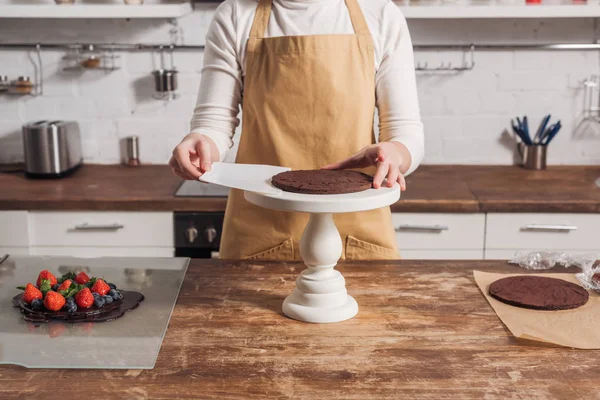 Tiro recortado de mujer en delantal preparando delicioso pastel dulce en la cocina - foto de stock