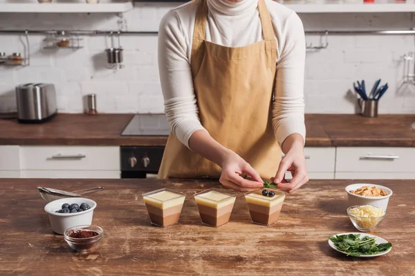 Section du milieu de la femme dans le tablier préparant triple dessert mousse au chocolat avec des bleuets — Photo de stock