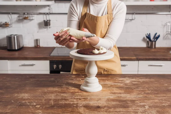 Tiro cortado de mulher em avental decorando bolo caseiro doce com creme — Fotografia de Stock