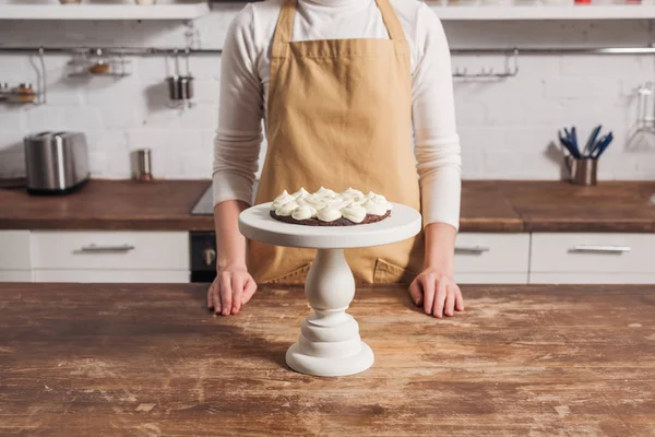 Середня частина жінки в фартусі готує смачний солодкий торт з вершками на кухні — стокове фото