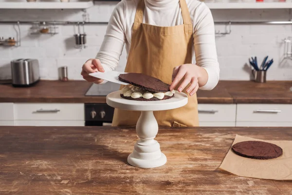 Средняя часть женщины в фартуке готовит изысканный сладкий торт на кухне — стоковое фото