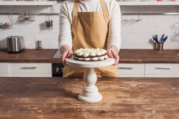 Colpo ritagliato di donna in grembiule cottura deliziosa torta dolce con crema — Foto stock