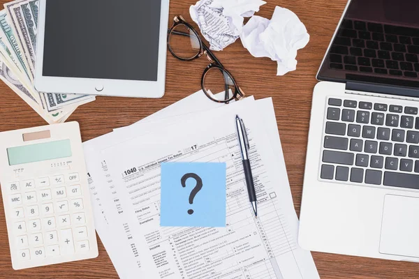 Top view of tax forms, digital devices and blue card with question mark on desk — Stock Photo