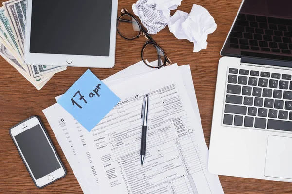 Top view of tax forms, digital devices and blue card with april 17 date on desk — Stock Photo