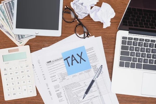 Top view of tax forms, digital devices and blue card with 'tax' word on desk — Stock Photo