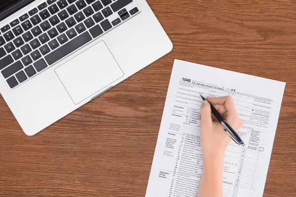 Vue recadrée de femme remplissant le formulaire d'impôt sur le lieu de travail avec ordinateur portable — Photo de stock