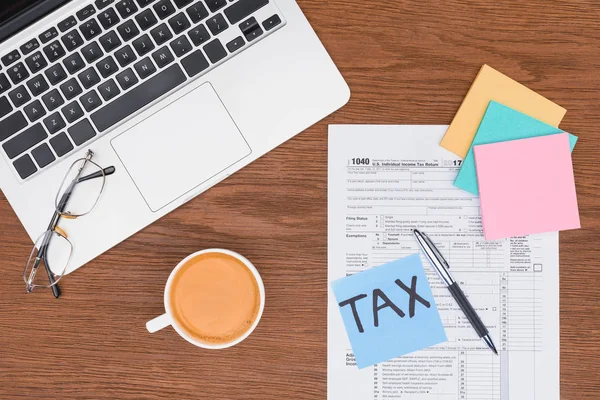 Top view of tax form, coffee, laptop and blue card with 'tax' word on desk — Stock Photo