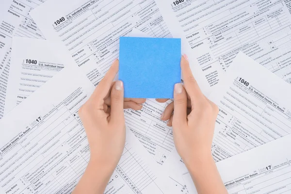 Cropped view of woman holding empty blue card with tax forms on background — Stock Photo