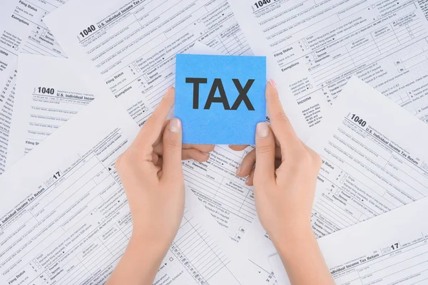 Cropped view of woman holding blue card with word 'tax' and documents on background — Stock Photo