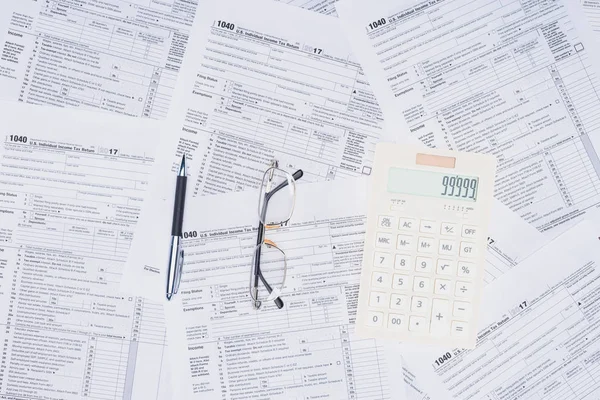 Vue du haut de la calculatrice, stylo et lunettes avec des formulaires d'impôt sur le fond — Photo de stock