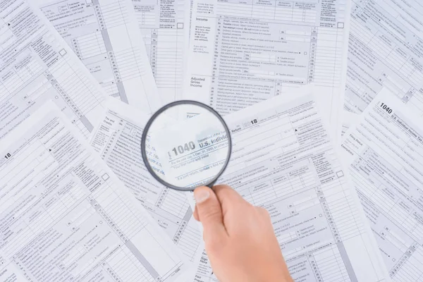 Cropped view of man holding magnifying glass over tax forms — Stock Photo