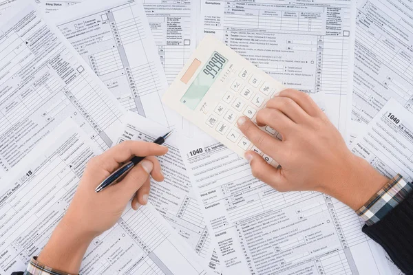 Vista recortada del hombre llenando formularios de impuestos y utilizando la calculadora - foto de stock