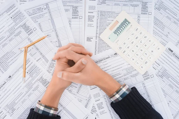 Cropped view of man with folded hands, broken pencil and calculator with tax forms on background — Stock Photo