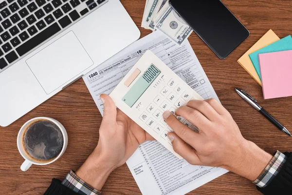 Vue recadrée de l'homme à l'aide d'une calculatrice avec formulaire d'impôt et ordinateur portable sur fond — Photo de stock