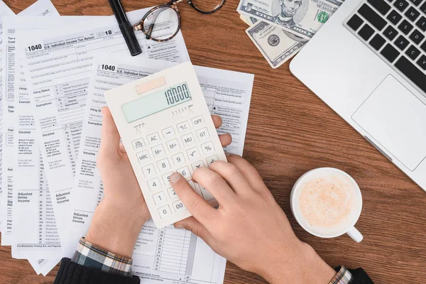 Vue recadrée de l'homme à l'aide d'une calculatrice avec des formulaires fiscaux et ordinateur portable sur fond — Photo de stock