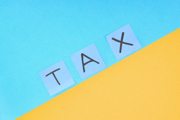 Vista superior de la palabra 'tax' hecha de tarjetas sobre fondo azul y amarillo - foto de stock
