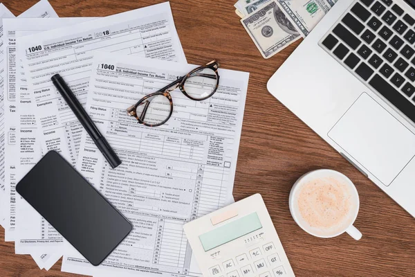 Vue en haut des formulaires fiscaux, du café, des appareils numériques et des billets de banque sur le bureau — Photo de stock