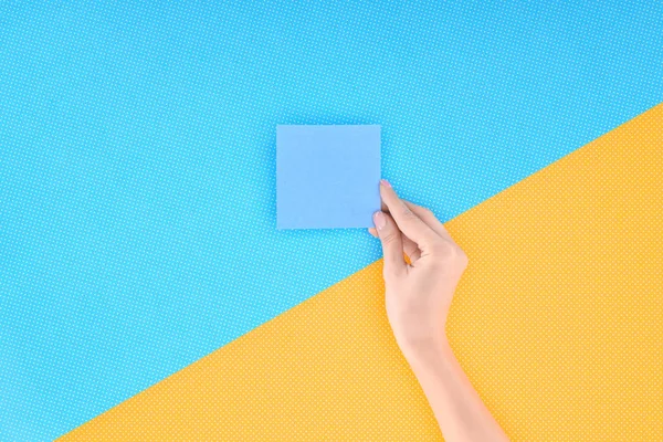 Vista recortada de la mujer sosteniendo la tarjeta azul vacía sobre fondo azul y amarillo - foto de stock