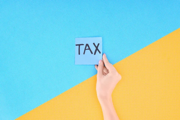 Cropped view of woman holding blue card with word 'tax' on blue and yellow background — Stock Photo