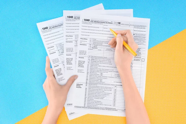 Partial view of woman filling tax forms on blue and yellow background — Stock Photo