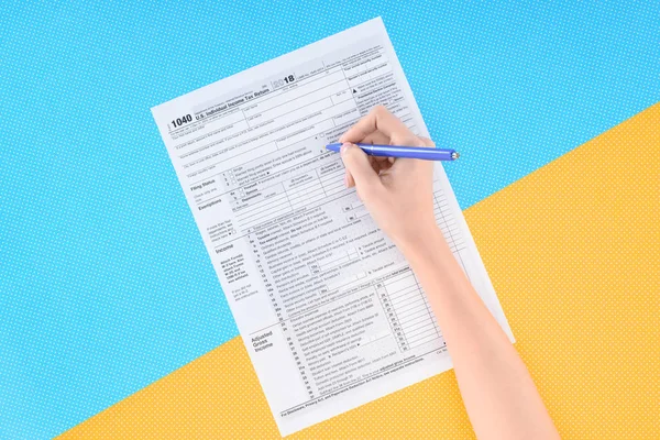 Vista cortada da mulher preenchendo formulário de imposto no fundo azul e amarelo — Fotografia de Stock