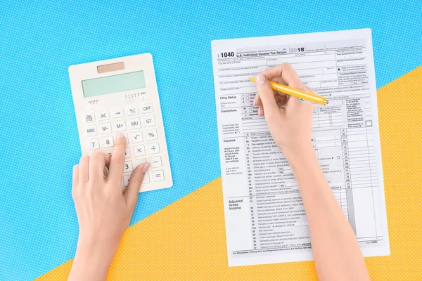 Vista recortada de la mujer utilizando la calculadora y llenar el formulario de impuestos sobre fondo azul y amarillo - foto de stock