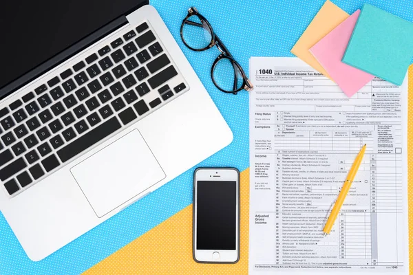 Top view of tax form and digital devices on blue and yellow background — Stock Photo