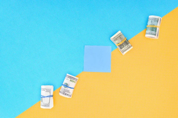 Vista superior de rollos de dinero y tarjeta vacía sobre fondo azul y amarillo - foto de stock