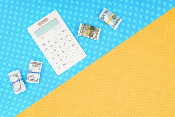 Vista superior de la calculadora y rollos de dinero sobre fondo azul y amarillo - foto de stock