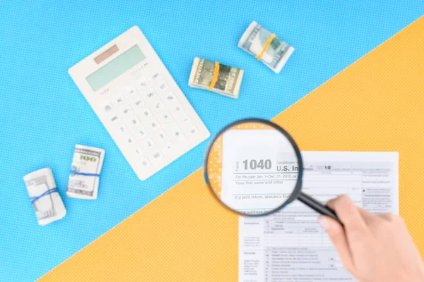 Cropped view of woman holding magnifying glass over tax form on blue and yellow background — Stock Photo